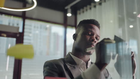 african american business man using sticky notes brainstorming problem solving strategy on glass whiteboard leader man showing solution for project deadline in office. bringing her vision