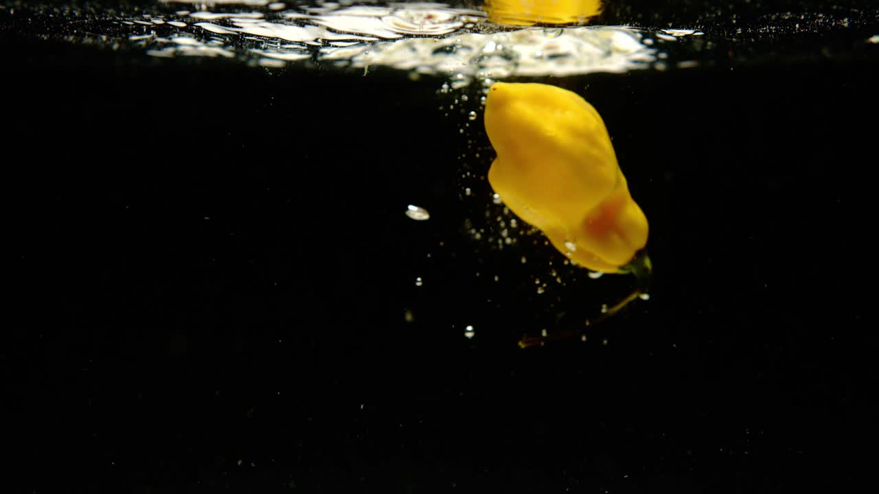 súper cámara lenta de fresca madame jeanette pimientos cayendo en el agua sobre fondo negro