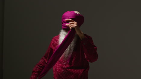 low key studio lighting shot of senior sikh man with beard tying fabric for turban against dark background 3