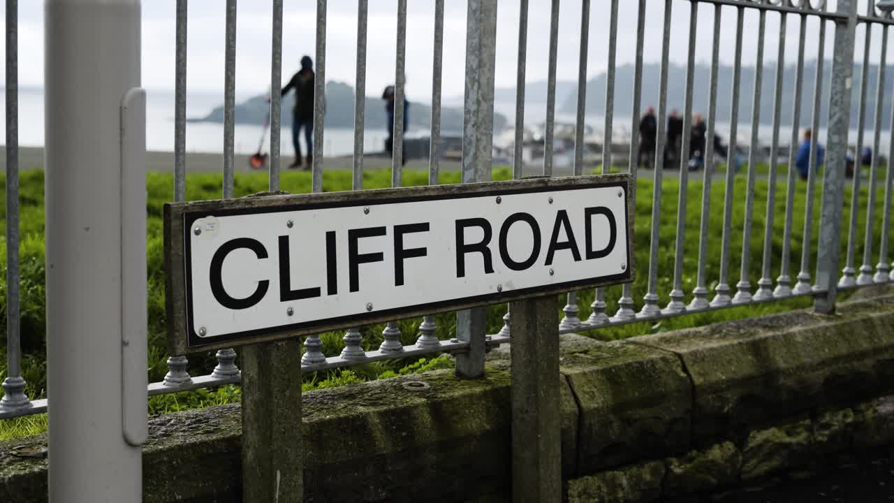 Cliff Road Sign On Steel Fence With People On The Background At Hoe Park In Plymouth, England