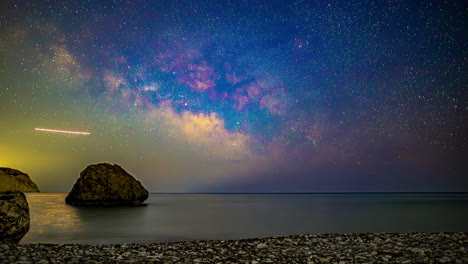 time lapse of the milky way and stars above the ocean and a rocky beach
