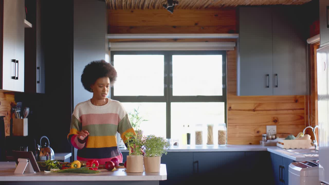 Happy african american woman preparing meal using tablet in sunny kitchen