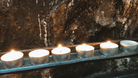 pan of candles in front of a rock wall