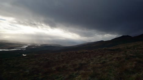 a panning shot slowly reveals a dark, moody landscape of mountains and lochs in the north west highlands of scotland as shafts of light pierce the sky in the distance