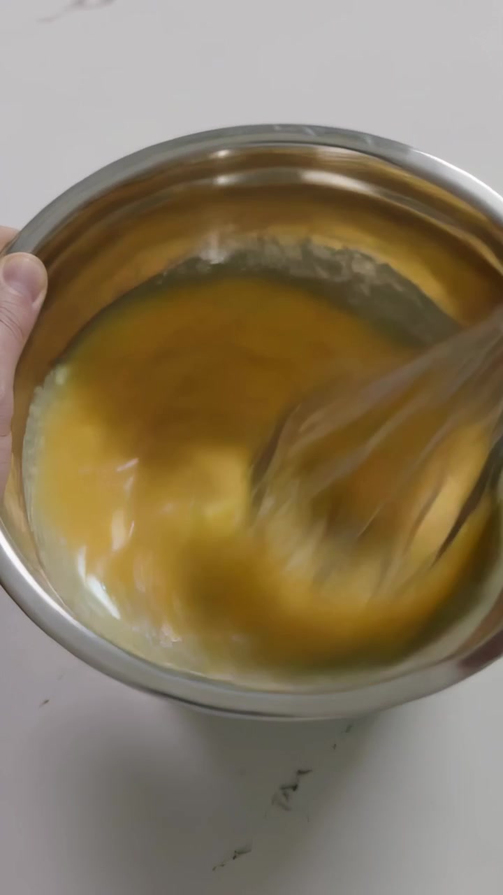 Vertical video: Whisking hands inserting whisk and aerating yellow batter in steel bowl in kitchen