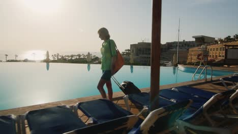 steadicam shot of woman with travel bag walking on recreation area along the pool