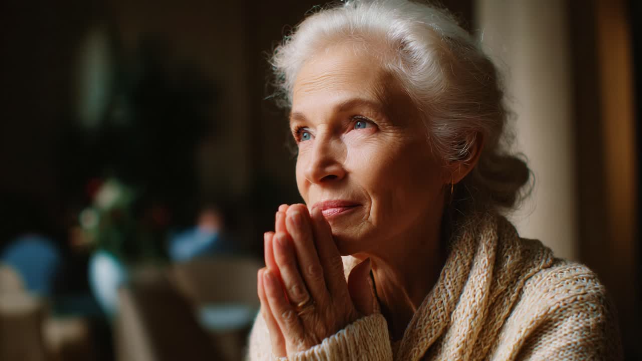 A contemplative woman with silver hair gazes thoughtfully out of the frame, reflecting on memories and emotions while clasping her hands together in deep thought, embodying a serene and introspective moment