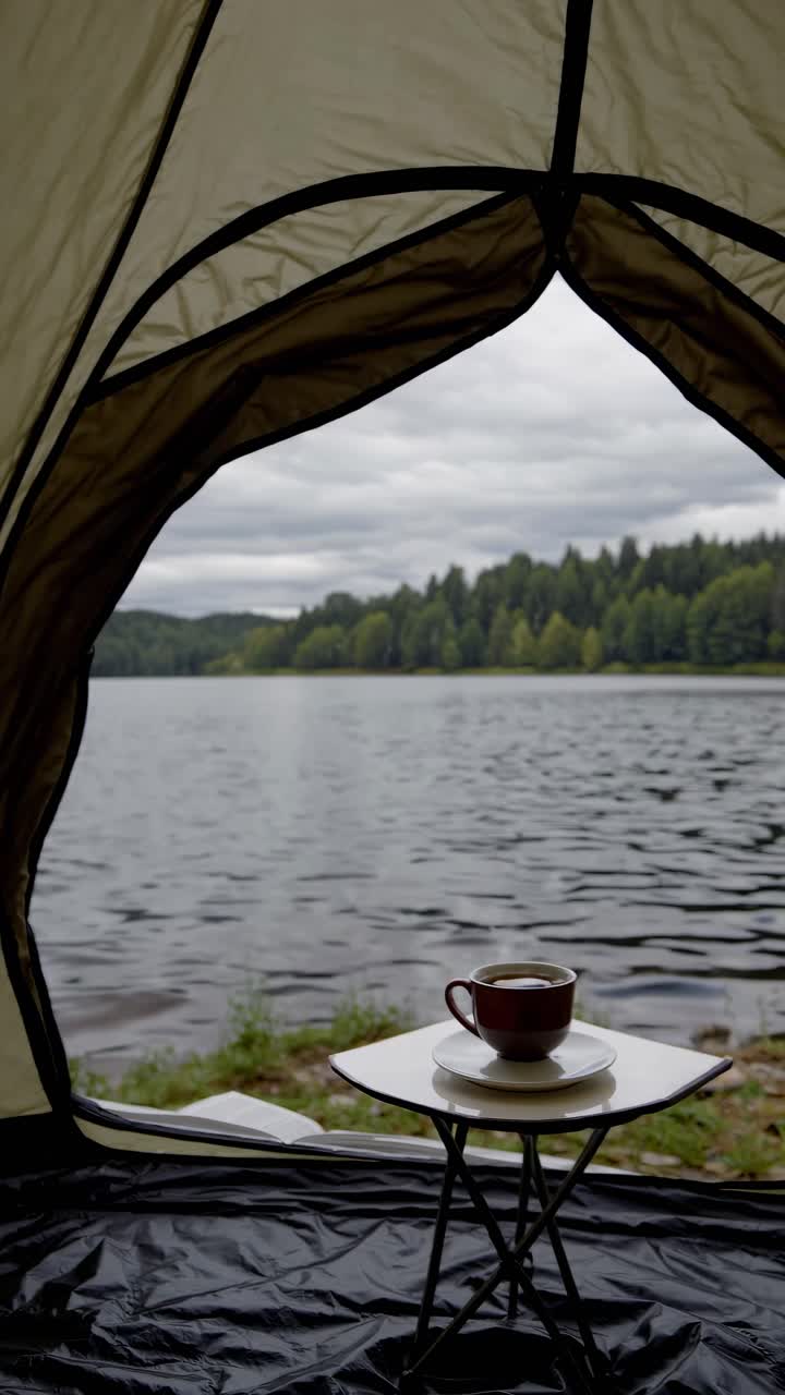 POV video angle from inside a tent, showcasing a serene lakeside view with a cup of coffee