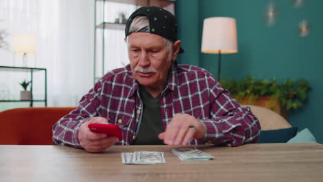 hombre mayor sonriente con dinero en efectivo y teléfono inteligente, satisfecho con los ingresos, planeando el presupuesto familiar
