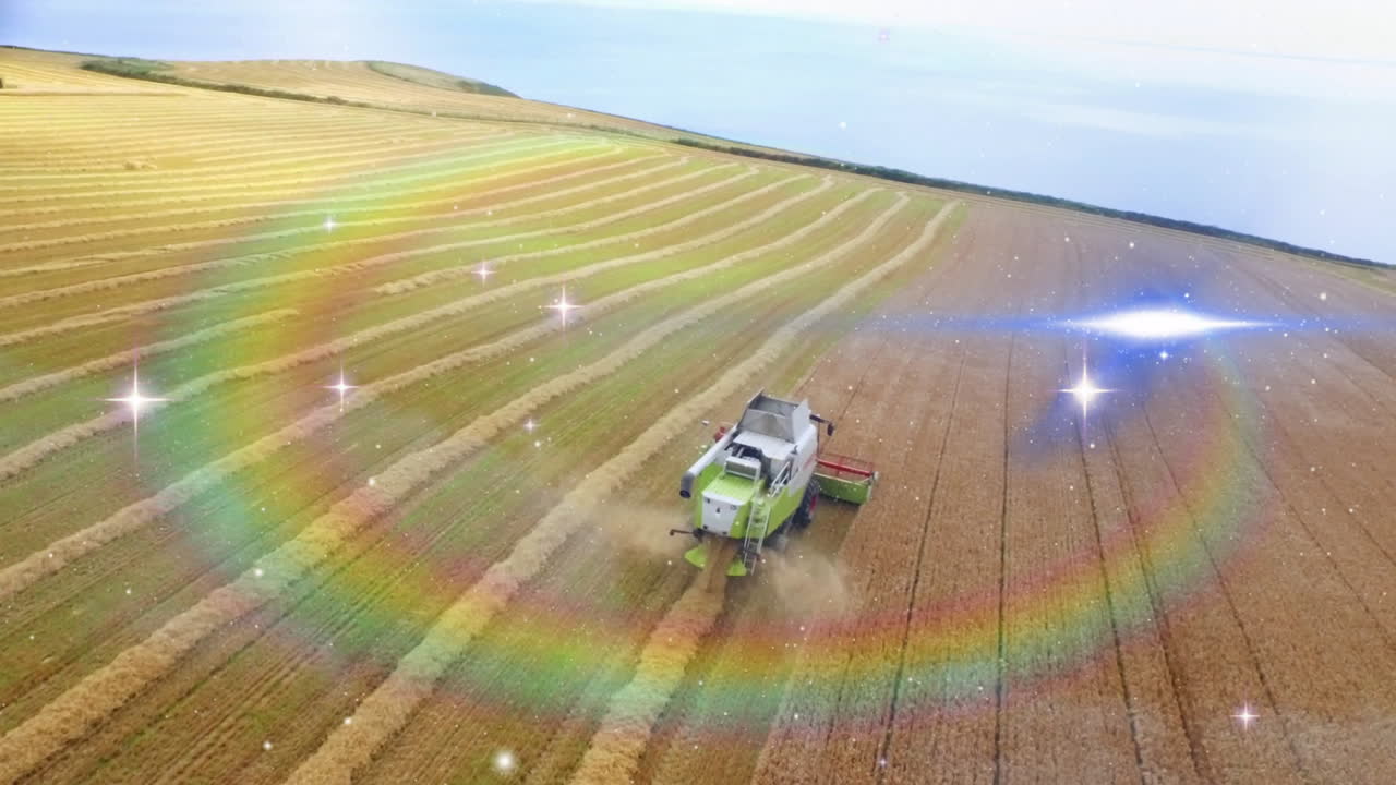 Combine harvester moving across aerial farmland, kicking dust plume under rainbow lens flares