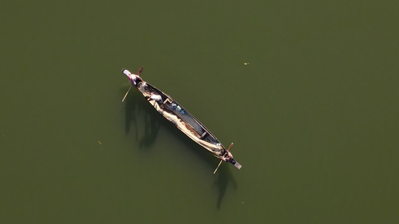 항공 영상은 큰 아시아 강에서 그물 낚시를 하는 나무 보트에 세 명의 어부를 포착합니다.