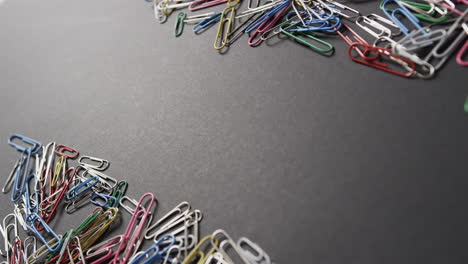 colorful paper clips are scattered on a dark gray surface, with copy space