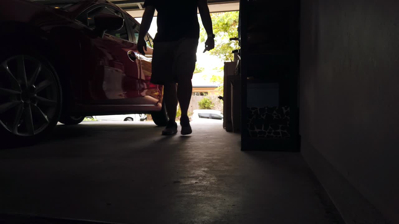 Silhouette of man walking behind red car in garage carport lit by light coming in from outside