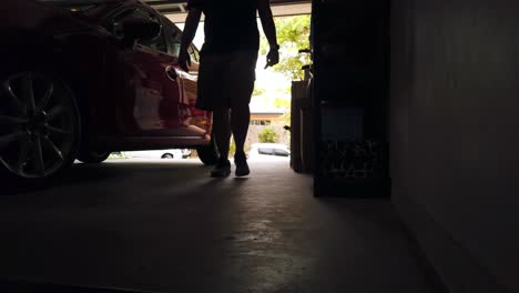 silueta de un hombre caminando detrás de un coche rojo en un garaje iluminado por la luz que entra desde el exterior