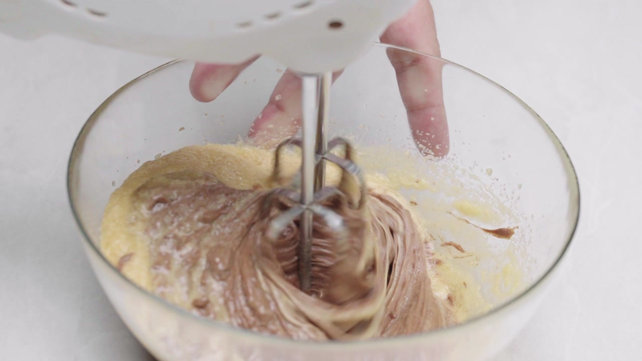 Close up slow motion of electric mixer blending cookie dough creating smooth swirl texture in bowl