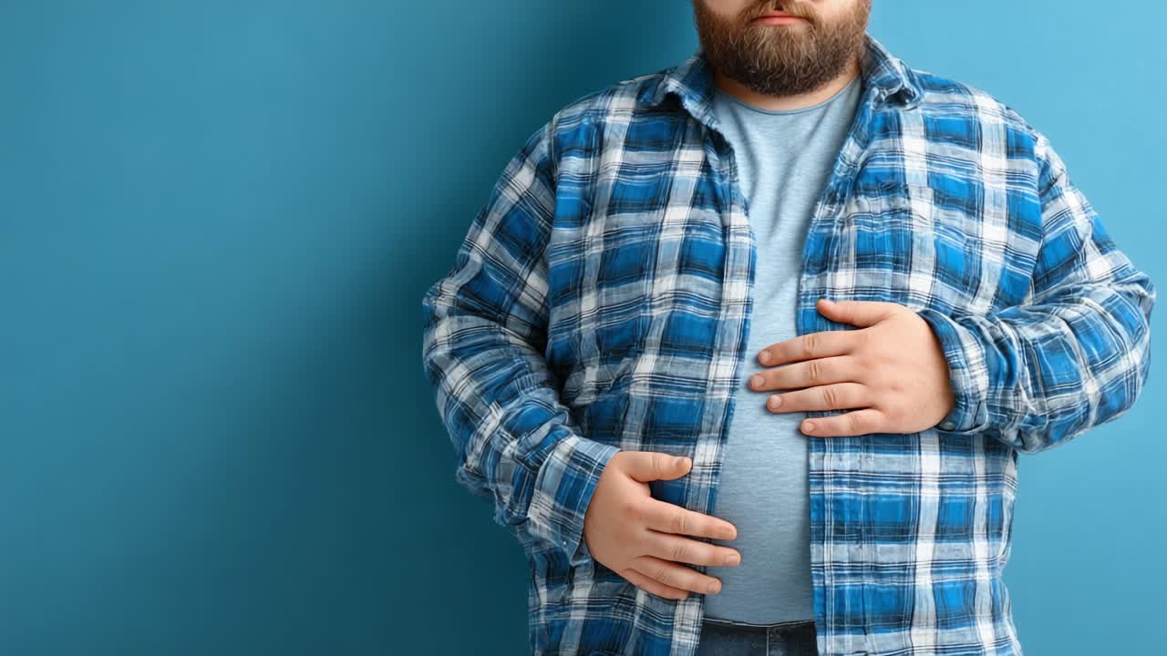 Un hombre con camisa a cuadros se sujeta suavemente el estómago, expresando incomodidad o saciedad sobre un fondo azul sólido, mostrando una emoción humana y conciencia corporal con las que es fácil identificarse