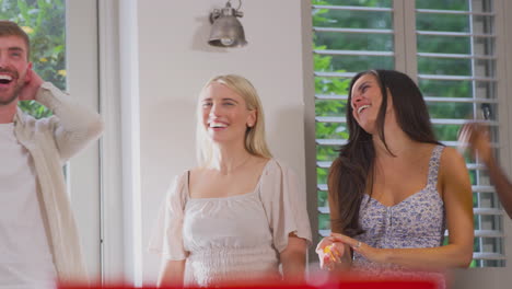 Multi-Cultural-Group-Of-Friends-Playing-Game-At-Home-Together-Throwing-Ball-Into-Paper-Cup