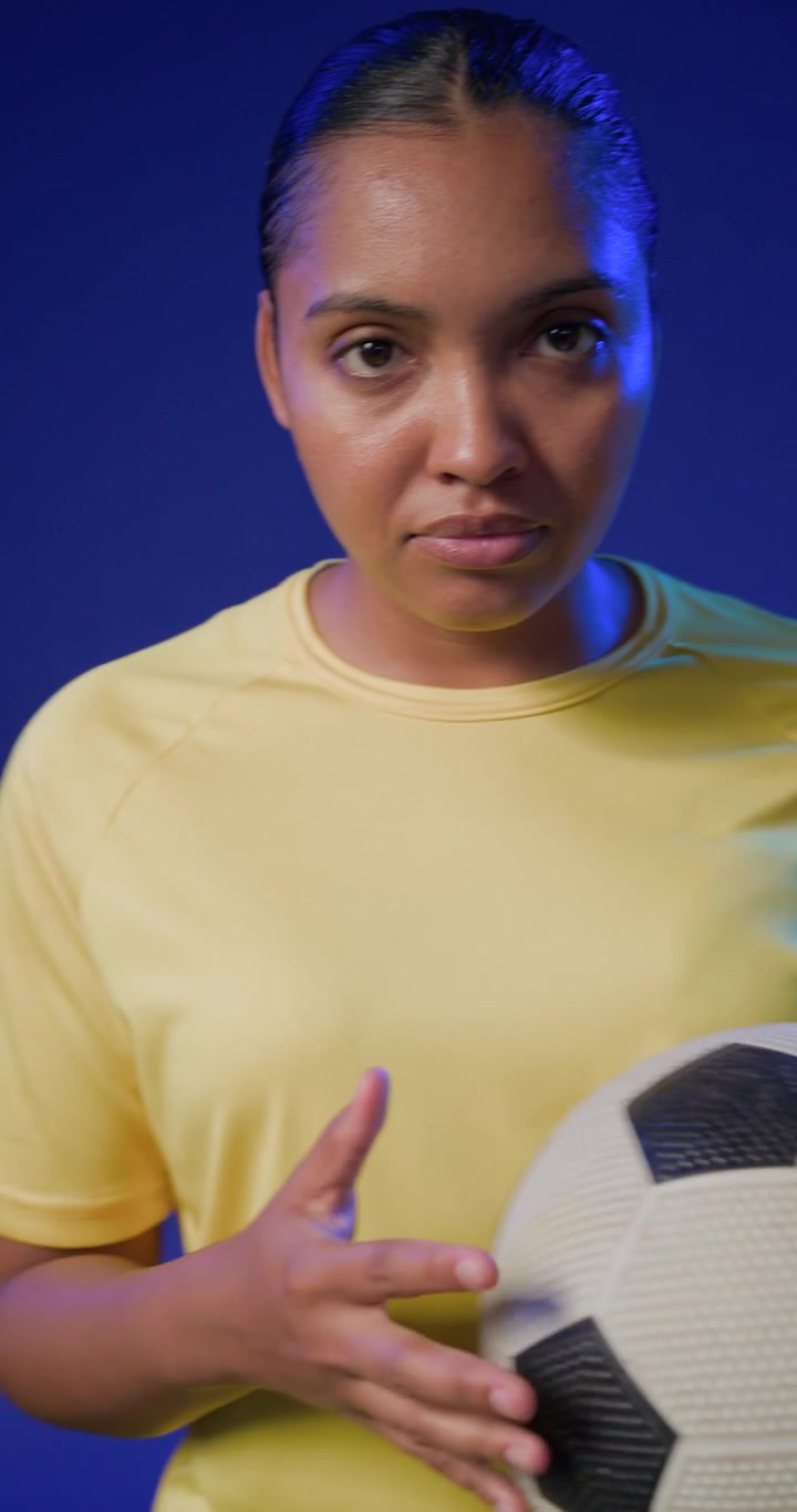 Donna afroamericana in maglietta gialla che si allunga verso un pallone da calcio proveniente da sinistra e si allena in studio.