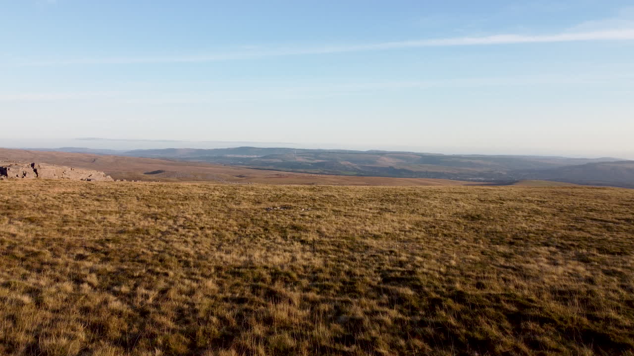 Aerial Drone Shot Moving Over Grass Mountain With Wind Farm and Fields in the Distance