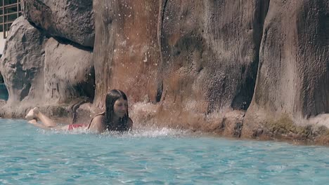 girl relaxes in red swimsuit under artificial waterfall