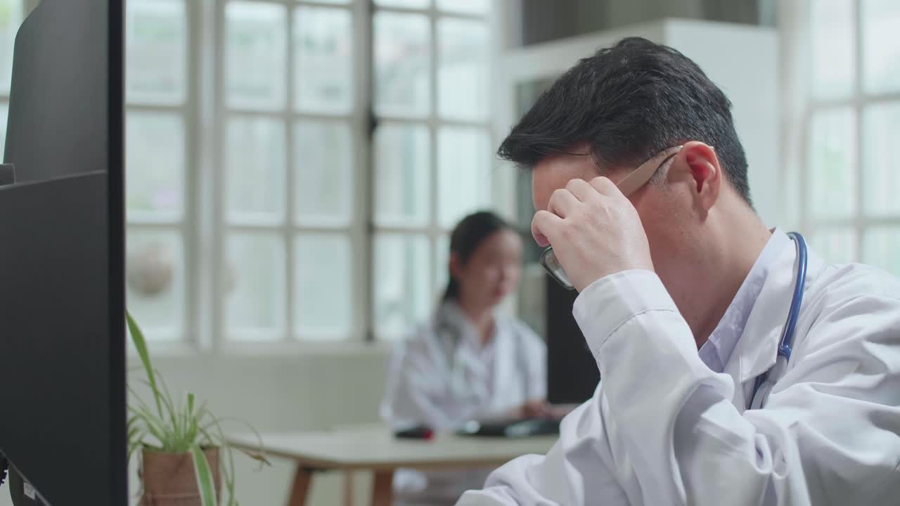 Asian Man Doctor Is Using Desktop Computer And Headache In Workplace. Medical Concept