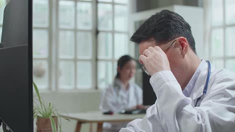 asian man doctor is using desktop computer and headache in workplace. medical concept