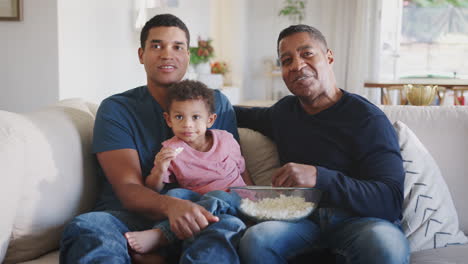 Drei-Generationen-Männliche-Familiengruppe-Sitzen-Auf-Einem-Sofa,-Essen-Popcorn-Und-Schauen-Gemeinsam-Fern