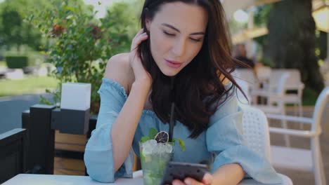 Hübsche-Brünette-Frau,-Die-Im-Restaurant-Im-Freien-Sitzt-Und-Ihr-Handy-Benutzt