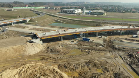 aerial view capturing the construction phase of a bridge overpass with the active site below, equipment in place, and nearby commercial buildings