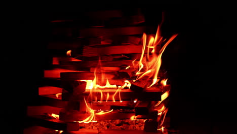 chopped wood in a big pile with small fire flames rising up. starting a campfire. darkness at backdrop.