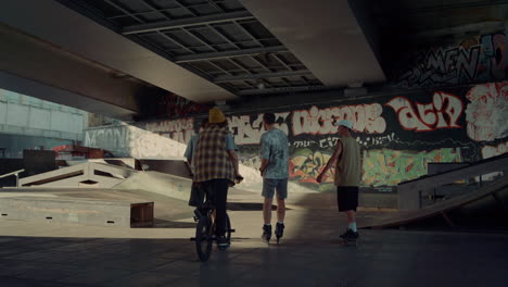 young riders talking together at skate park graffiti. active friends riding