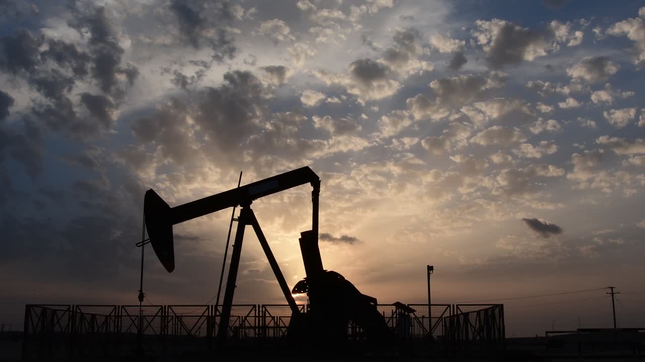 Silhouette of crude oil pump standing still  in the oilfield at cloudy sunset