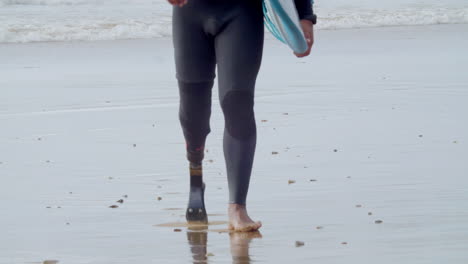 close up of an unrecognizable man in wetsuit with bionic leg walking along the seashore 1