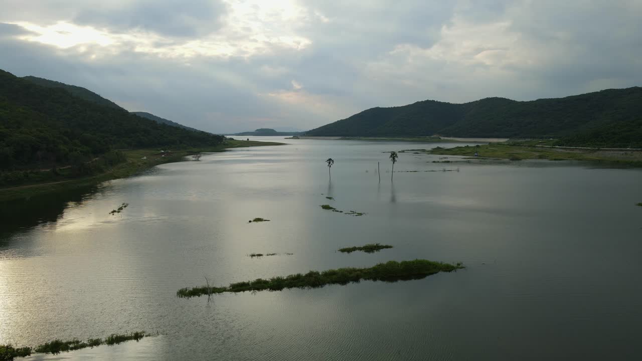Reverse aerial footage of a lake and sunset revealing palm trees in the middle and bars of land showing the whole picture, Muak Klek, Saraburi, Thailand