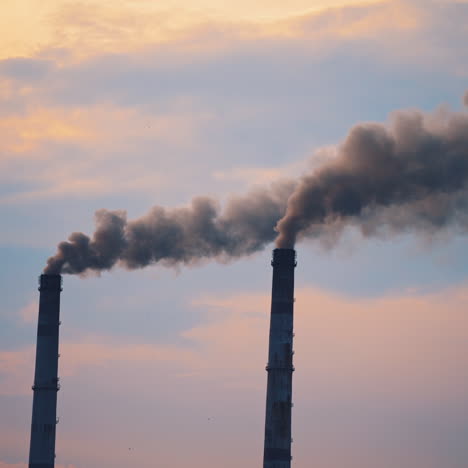 Air pollution by smoke coming out of two factory chimneys. Smoking pipes against the sky. Ecological disaster, air pollution. Environmental problems badly affecting life.
