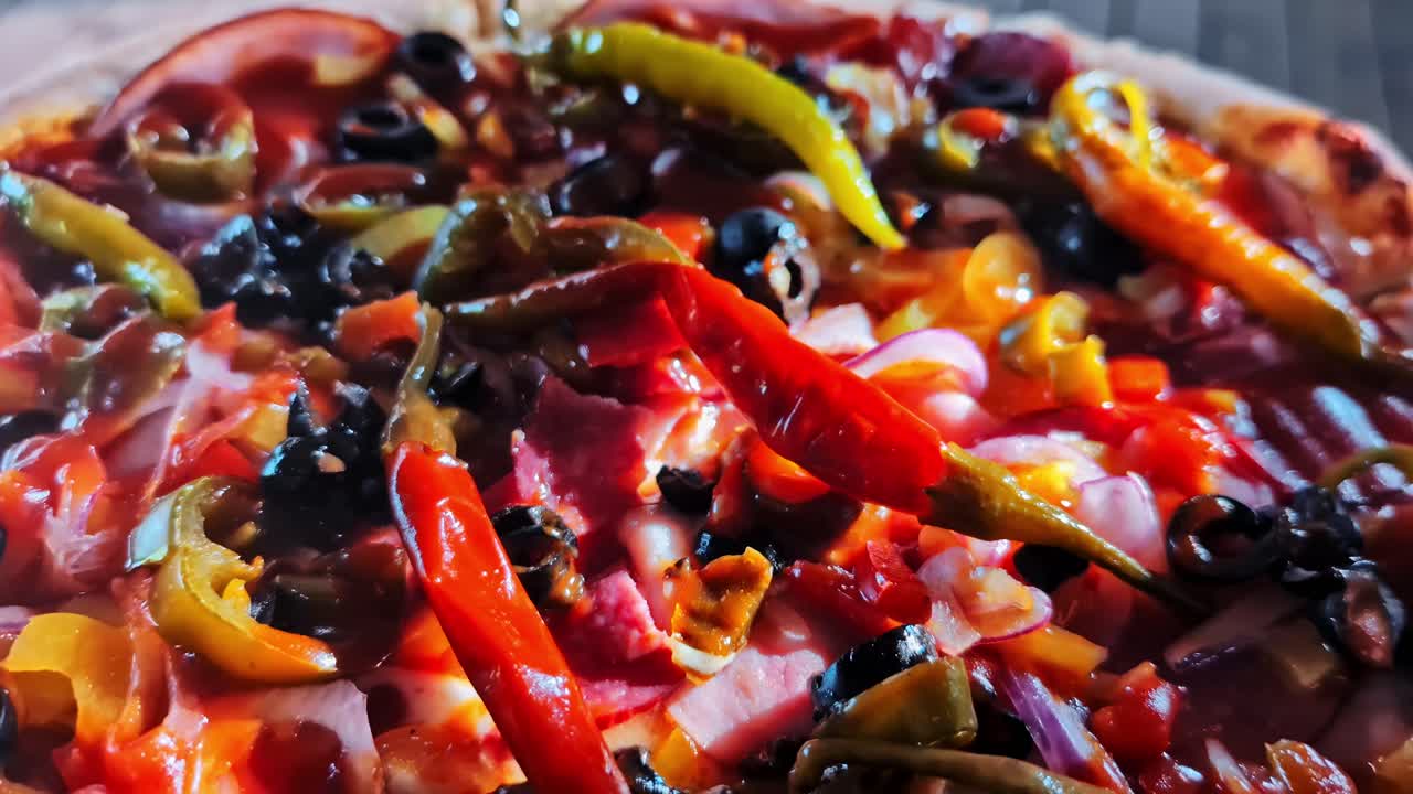 Reveals a delicious freshly baked pizza with pepperoni, olives, and a variety of spicy peppers on a wooden table - Slow motion pull back