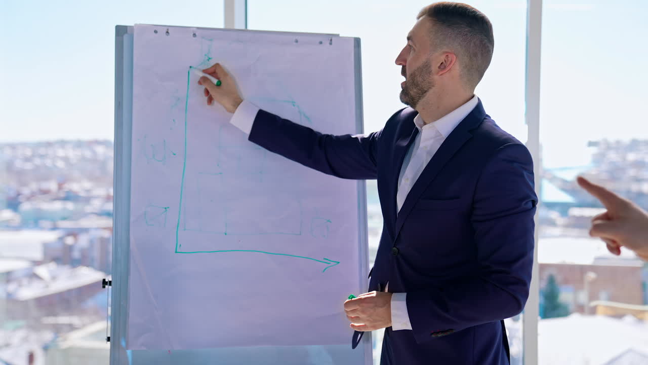 Manager is drawing on whiteboard in light office. Handsome businessman in suit showing his new strategy on city window background. Business concept.