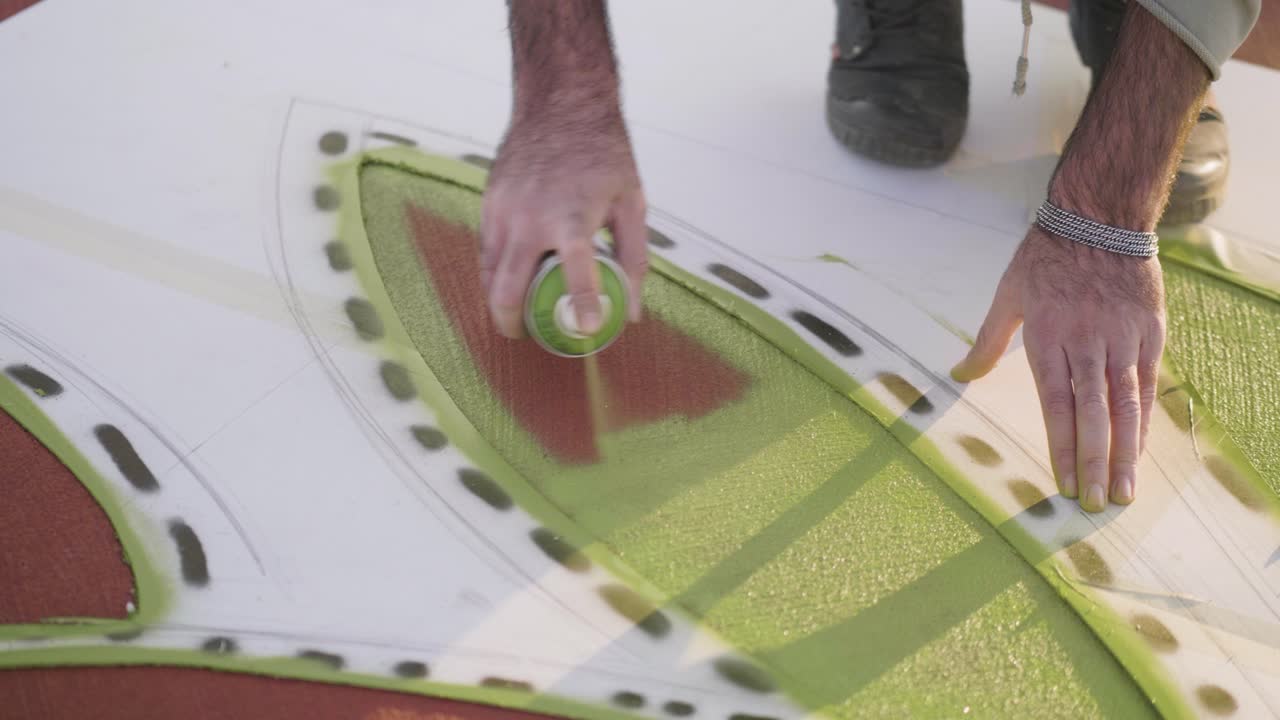 Spray paint artist painting a vibrant green design on a large canvas outdoors