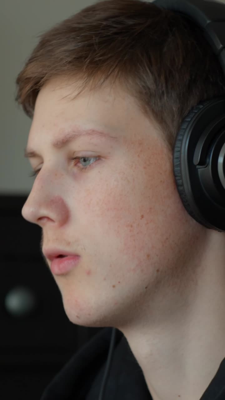 Young caucasian man listening with headphones, adjusting an earcup, engaging with content, enjoying music or podcast, focusing on sound and digital audio in close up profile, vertical shot