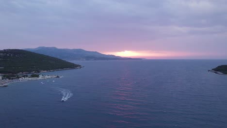 aerial view of boat travelling over ionian sea with orange sunset in horizon