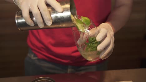 barman pours mojito from mixer into glass, slow motion