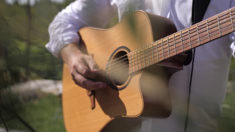 man playing guitar, closeup handheld shot, outdoors sunny summer day, picking strings