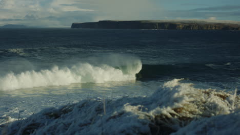 and ice covers coastal grass as ocean waves catch early morning light below cliffs as surfers chase waves, slow motion