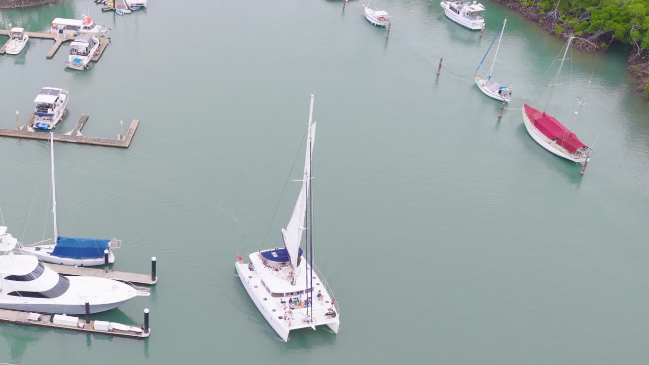 Aerial footage captures boats docked in a serene marina with calm waters and lush greenery, under soft daylight