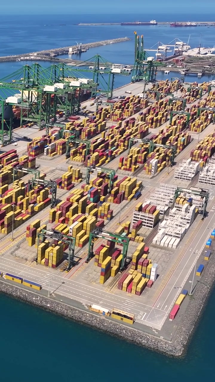 A busy container terminal filled with shipping containers. Crane operations are visible as cargo is loaded and unloaded. The terminal plays a key role in global shipping and trade.