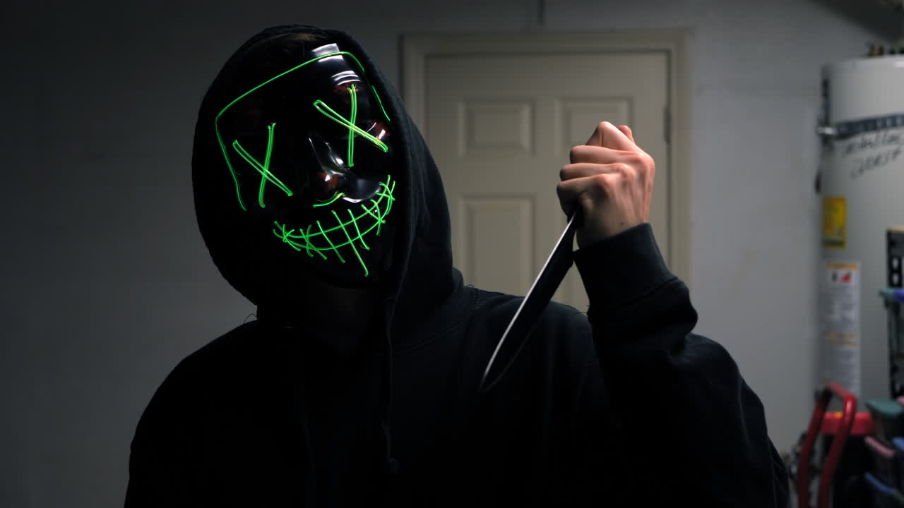 un asesino aterrador con una máscara genérica de terror de halloween tirando un cuchillo a su víctima de asesinato