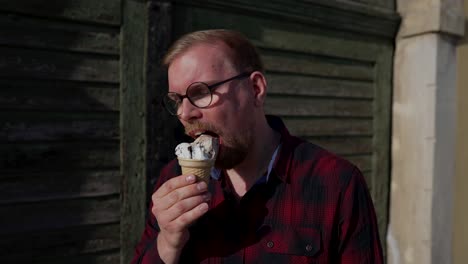 young man with glasses eats ice cream in cone, sunny day outside