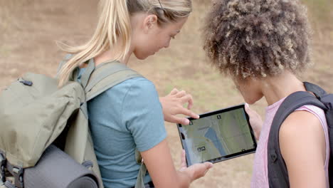 Young-Caucasian-woman-and-biracial-woman-are-examining-a-tablet-outdoors