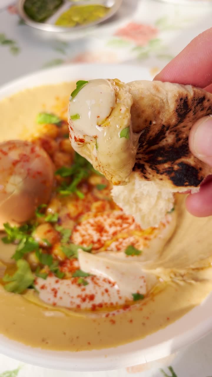 POV: intingere pane pita nell'hummus in un tipico ristorante mediterraneo in Medio Oriente. Punto di vista di un buongustaio o turista che mangia la tradizionale salsa di ceci in Israele su un tavolo. Delizioso, sano, vegano. UGC.
