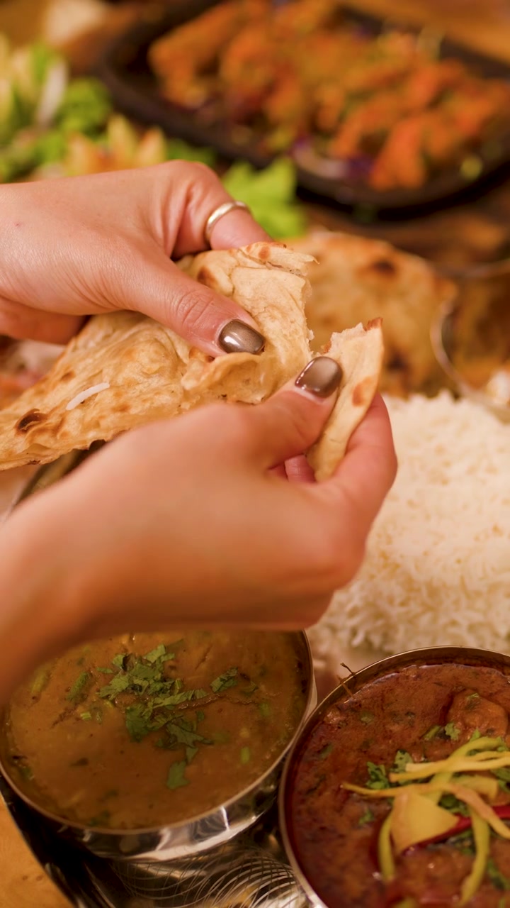 Primer plano de manos rompiendo pan plano sobre una variada comida india con curry y arroz.